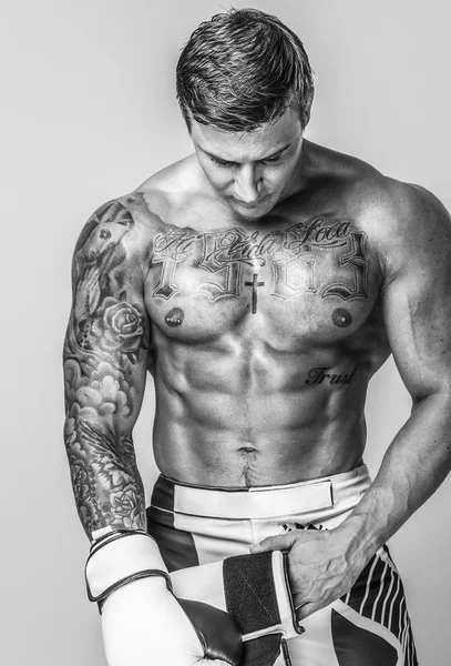 A muscled and tattooed man is putting on boxing gloves — Stock Photo, Image