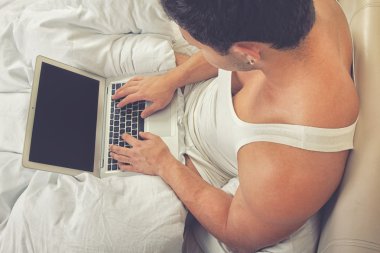 Adam yatakta otururken, dizüstü bilgisayar kullanarak