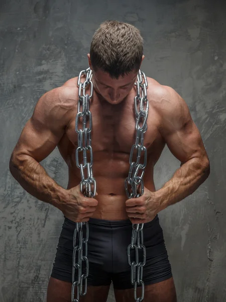 Big bodybuilder showing his body and holding steel chain — Stock Photo, Image