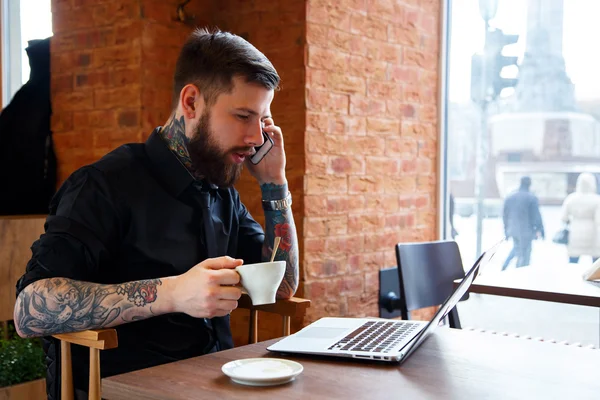 Male with tattoes talking on a phone in coffee shop — Stock Photo, Image