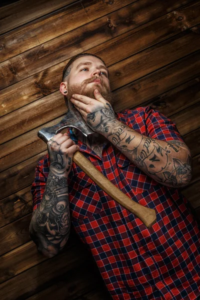 Omul tatuat atârnă toporul pe fundal din lemn . — Fotografie, imagine de stoc