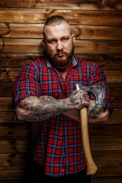 Hombre tatuado cuelga hacha sobre fondo de madera . — Foto de Stock