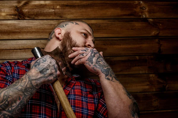 Tatuado homem pendurar machado no fundo de madeira . — Fotografia de Stock