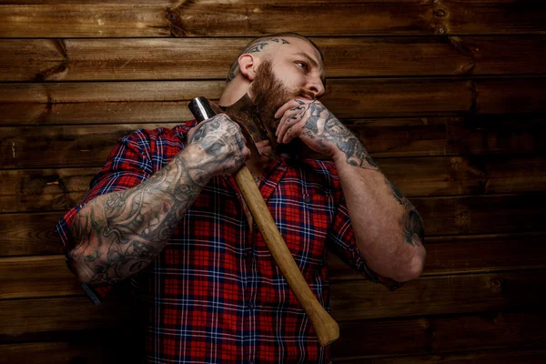 Hombre tatuado cuelga hacha sobre fondo de madera . —  Fotos de Stock