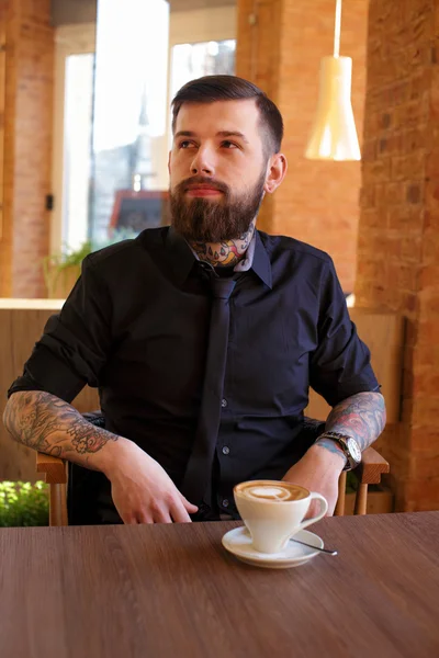 Mann mit Tätowierungen trinkt Kaffee. — Stockfoto