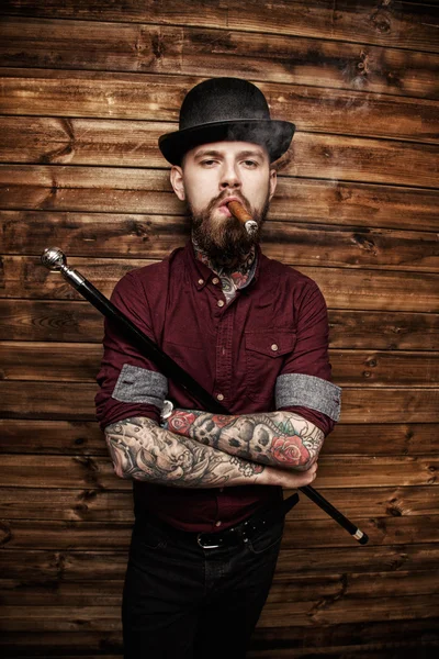 Hombre con tatto fuma y sostiene bastón — Foto de Stock