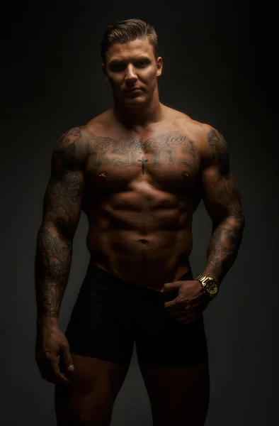 Muscular man with tattooes in deep shadows — Stock Photo, Image