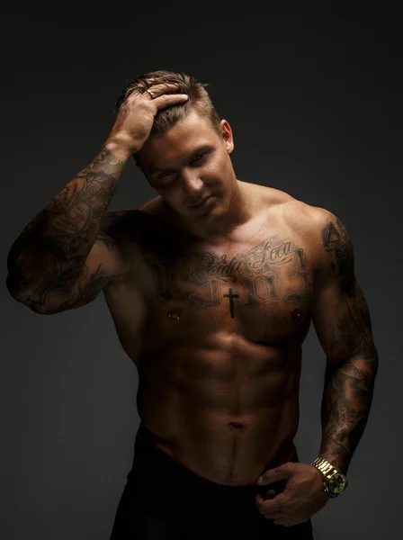 М'язистий чоловік з татуюваннями в глибоких тінях — стокове фото