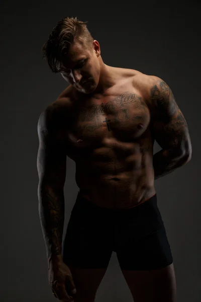 Muskularny mężczyzna z tattooes w głębokich cieni — Zdjęcie stockowe