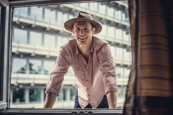 Smiling guy in big hat looking through window. — Stock Photo, Image