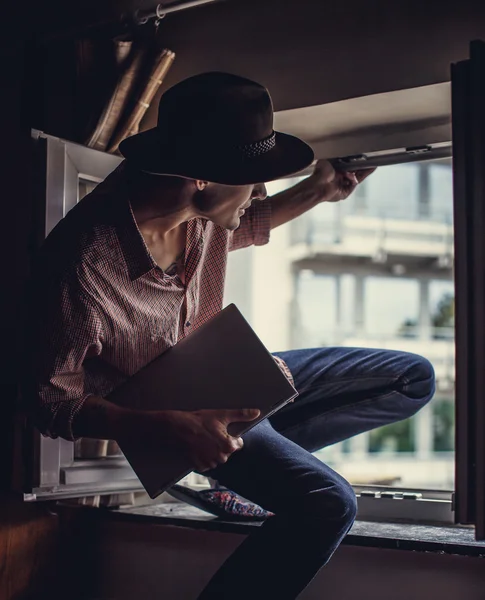 Un tipo con sombrero grande sentado en la ventana — Foto de Stock