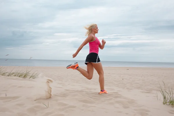 Donna bionda sportiva che corre sulla spiaggia — Foto Stock