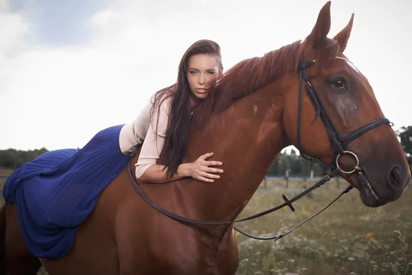 Дівчина моди в довгій блакитній сорочці лежить на коричневому коні над білим — стокове фото