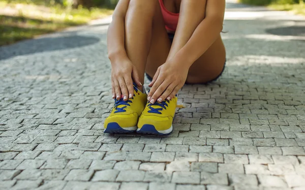 Frauenbeine in gelben Sportschuhen auf grauem Untergrund. — Stockfoto