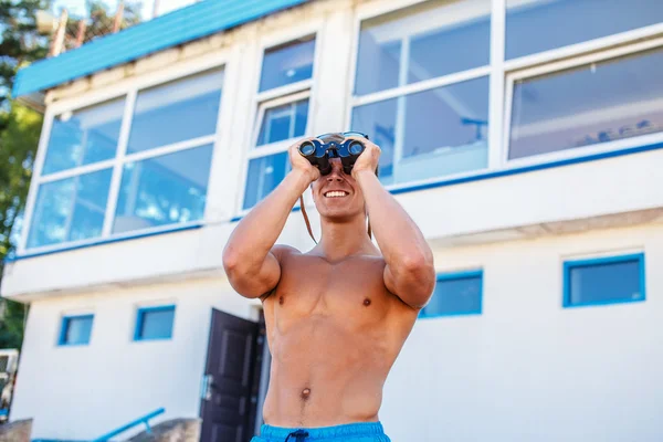 Shirtless muscular sea rescuer looking in binocular. — Stock Photo, Image