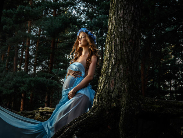 Artistic portrait of pregnant woman in blue fluttering dress.