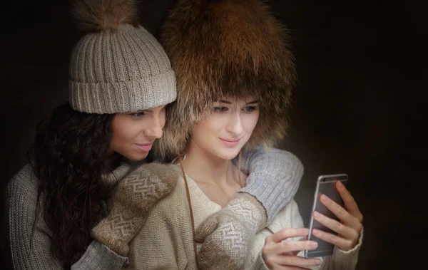 Duas meninas em roupas de inverno wathing imagens no smartphone . — Fotografia de Stock