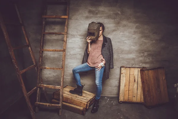 Casual woman in blue jeans holds welder mask.