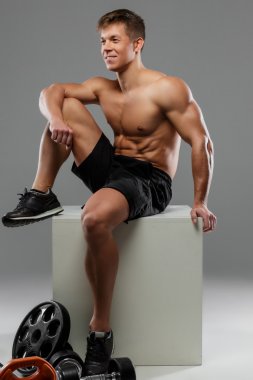 Gömleksiz kas adam beyaz kutu üzerinde oturur.