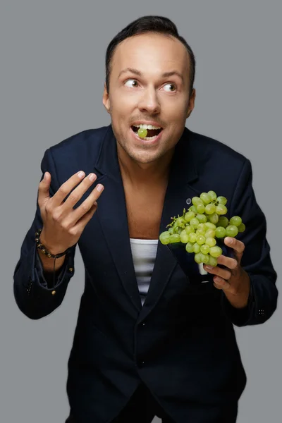 Um homem de fato azul a segurar uvas verdes . — Fotografia de Stock