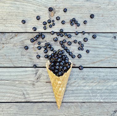 Gözleme koni rustik ahşap arka plan üzerinde siyah kuş üzümü. Diyet ve sağlıklı tatlı. Yukarıdan, vintage renk, düz stil yatıyordu