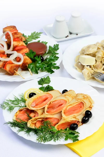 White table with food of meat, salmon rolls and dumplings. — Stock Photo, Image