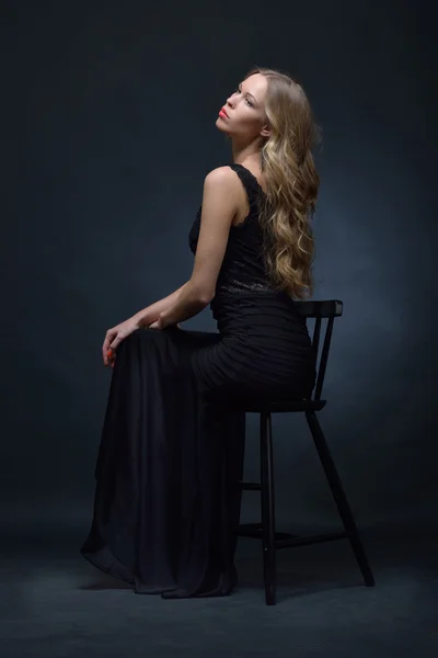 Beautiful woman in a black evening dress posing with chair — Stock Photo, Image