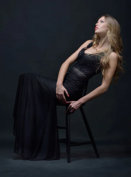 Sandalye ile poz siyah gece elbisesi içinde güzel bir kadın Stok Resim