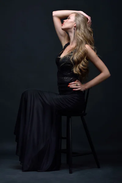 Mulher bonita em um vestido de noite preto posando com cadeira — Fotografia de Stock