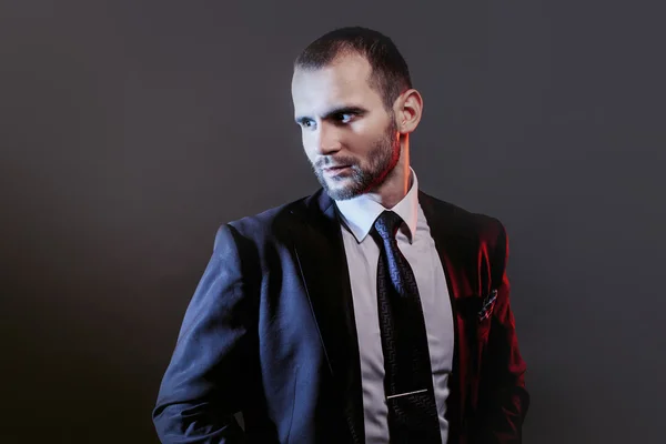 Σοβαρός άνθρωπος σε ένα επαγγελματικό κοστούμι, σκούρο φόντο, μπλε και κόκκινους τόνους οπίσθιου φωτισμού — Φωτογραφία Αρχείου
