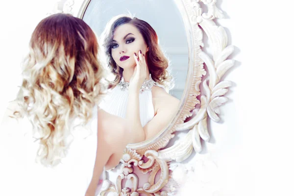 Portrait of young sexy woman in a white dress looking at the mirror. High key soft image — Stock Photo, Image