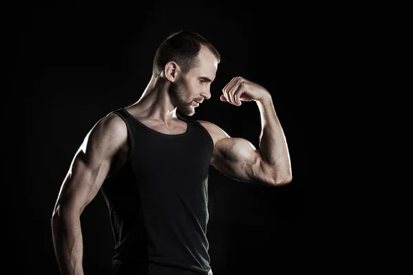 Muscular man,  shows his biceps, black background, place for text on the right — Stock Photo, Image