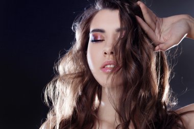 Uzun dalgalı saçlı güzel genç esmer kız. Kıvırcık saç modeli. Siyah arka plan
