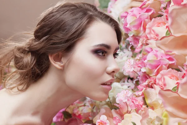 Πορτρέτο του το όμορφο κορίτσι μόδας, μυρίζοντας μια πολλά λουλούδια. Υπέροχο μακιγιάζ και βρώμικο ρομαντική χτένισμα. Λουλούδια φόντο. Πράσινα μάτια. — Φωτογραφία Αρχείου