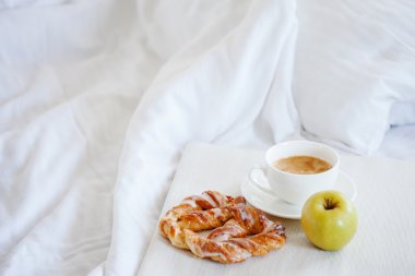 Bir yatakta kahvaltı tepsisiyle. Tatlı tuzlu kraker, kahve ve elma