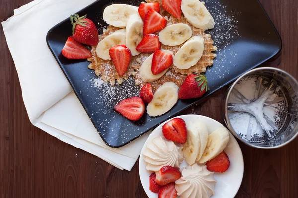 Waffles com morangos frescos e bananas em fundo de madeira rústica. Vista superior — Fotografia de Stock