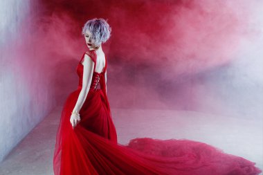 Kırmızı elbiseli genç muhteşem kadın moda fotoğrafı. Dokulu arka plan, duman