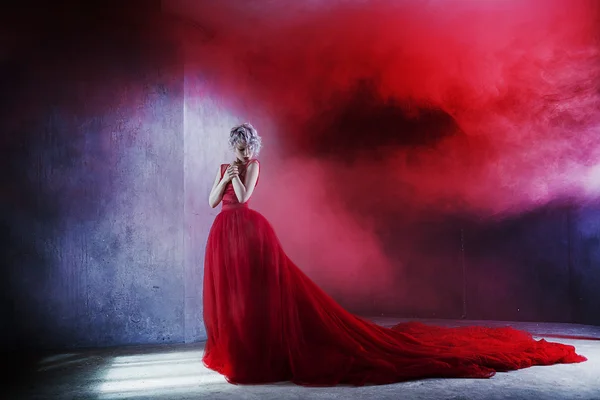 Foto de moda de jovem mulher magnífica em vestido vermelho. Fundo texturizado, fumaça vermelha — Fotografia de Stock