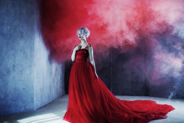 Kırmızı elbiseli genç muhteşem kadın moda fotoğrafı. Dokulu arka plan, duman