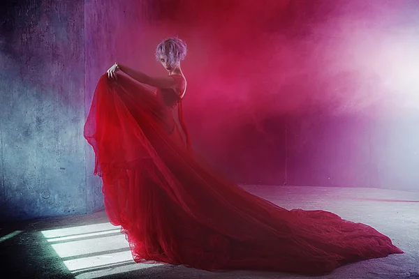 Fashion photo of young magnificent woman in red dress. Textured background, smoke — Stock Photo, Image