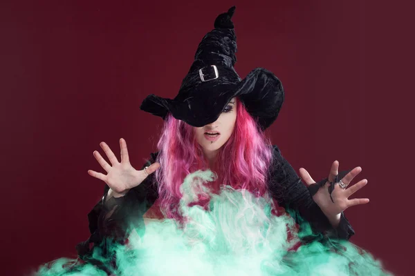 Scary witch with red hair performs magic over the green smoke . Halloween, horror theme. — Stock Photo, Image