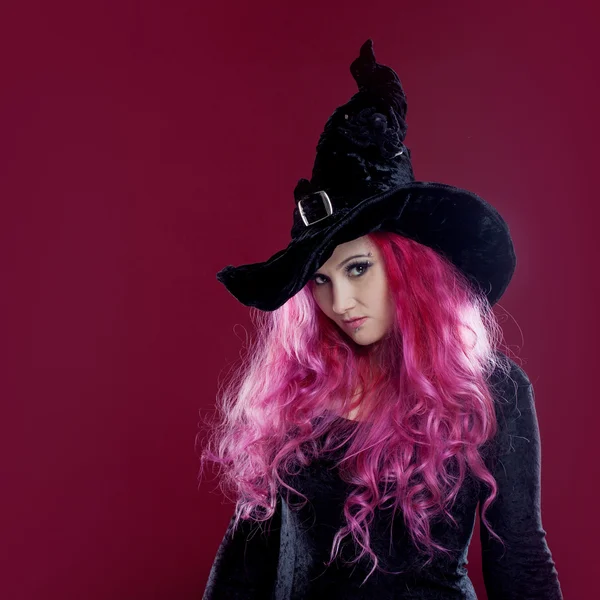 魔女帽子と赤い髪と衣装で魅力的な女性は、ピンクの背景の魔法を実行します。ハロウィーン、ホラーのテーマ. — ストック写真
