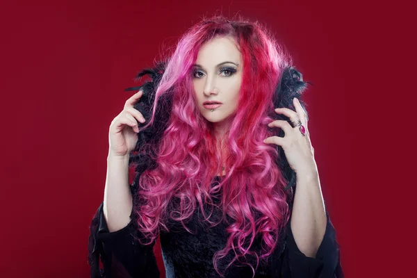 Atrakcyjna czarownica z czerwonymi włosami wykonuje magię na różowym tle. Halloween, horror motyw. — Zdjęcie stockowe