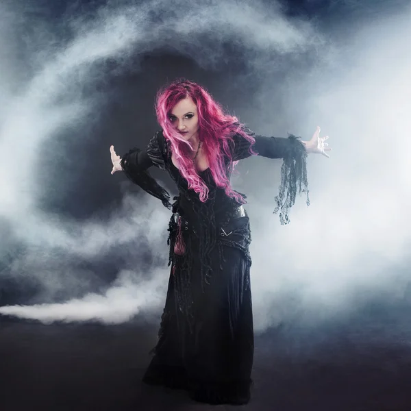 Halloween Witch creates tornado. Attractive woman with red hair in witches costume standing outstretched arms, strong wind — Stock Photo, Image