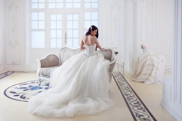 Mooi meisje bruid in een prachtige jurk die zittend op de Bank. Luxe, lichte interieur — Stockfoto