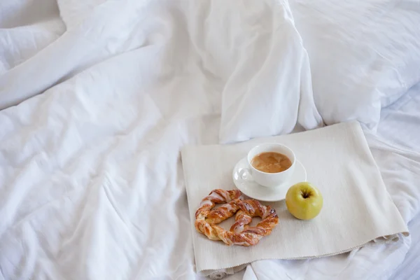 Bandeja com café da manhã em uma cama. Doce pretzel, xícara de café e maçã — Fotografia de Stock