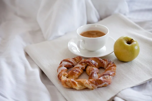 Tray with breakfast on a bed. Sweet pretzel, Cup of coffee and Apple — Stock Photo, Image