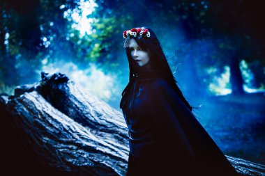 Karanlık ormanın içinde bir kukuleta ile genç siyah saçlı kız uzun pelerin içinde. Tonlama etkisi