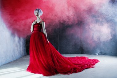 Kırmızı elbiseli genç muhteşem kadın moda fotoğrafı. Dokulu arka plan, duman