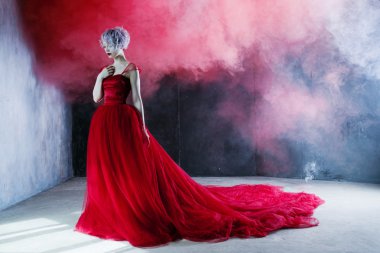 Kırmızı elbiseli genç muhteşem kadın moda fotoğrafı. Dokulu arka plan, duman